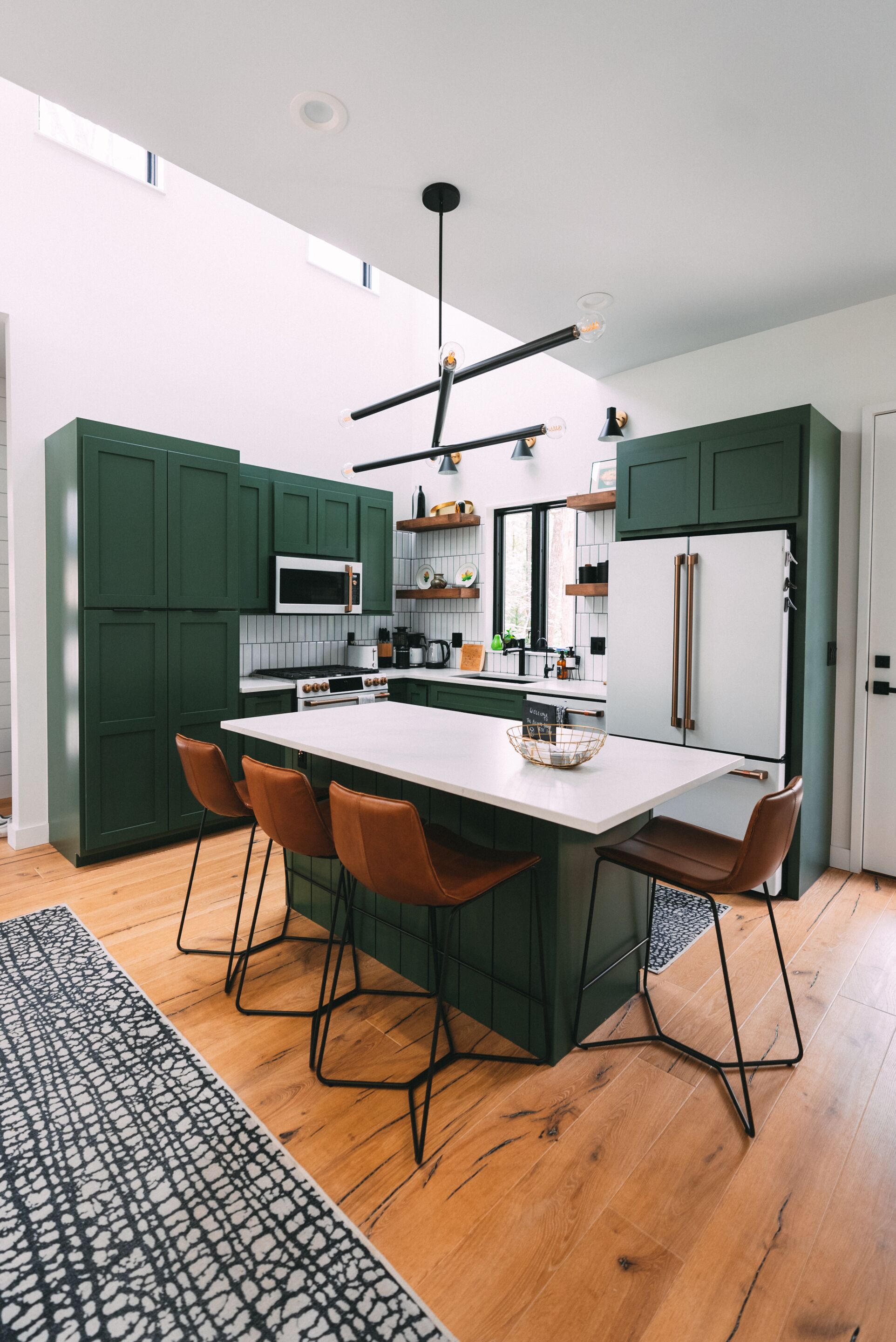 Een moderne keuken met groene kastjes, een wit aanrechtblad en een centraal eiland met barstoelen.