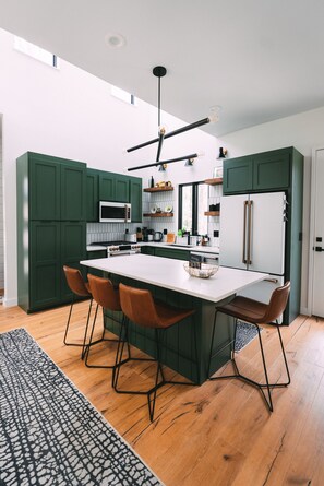 Una cocina moderna con gabinetes verdes, una encimera blanca y una isla central con taburetes de bar.