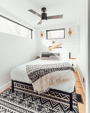 A modern bedroom with a bed, a ceiling fan, a window, and a patterned rug.
