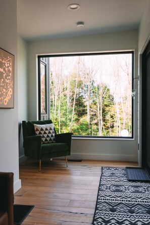 Una habitación moderna con un ventanal grande, un sofá verde, un tapete estampado y una puerta que da al exterior.