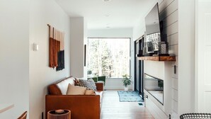 A modern living room with a wooden floor, a sofa, a coffee table, and a dining area with a wooden table and chairs.