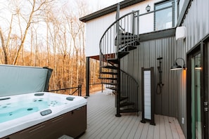 A hot tub on a wooden deck with a spiral staircase leading to a second floor.