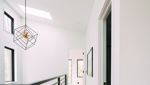 A modern interior with a wooden floor, black railing, and a geometric pendant light.