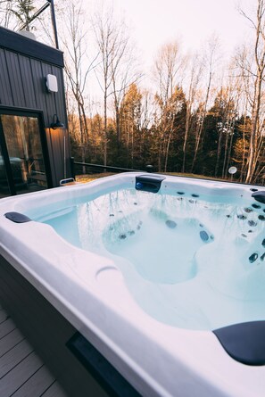 A hot tub with a wooden deck and a glass enclosure, surrounded by trees.