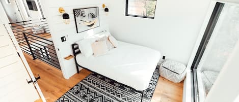 Un dormitorio moderno con una cama blanca, un tapete estampado y un ventanal grande.