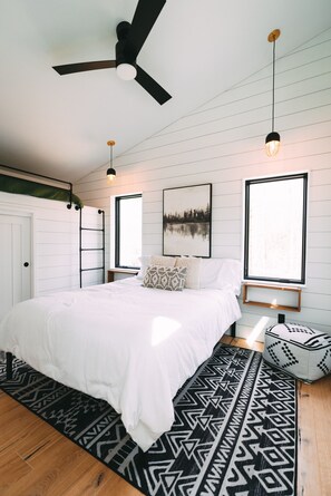 A bedroom with a bed, a ceiling fan, two pendant lights, a window, and a wall-mounted picture.