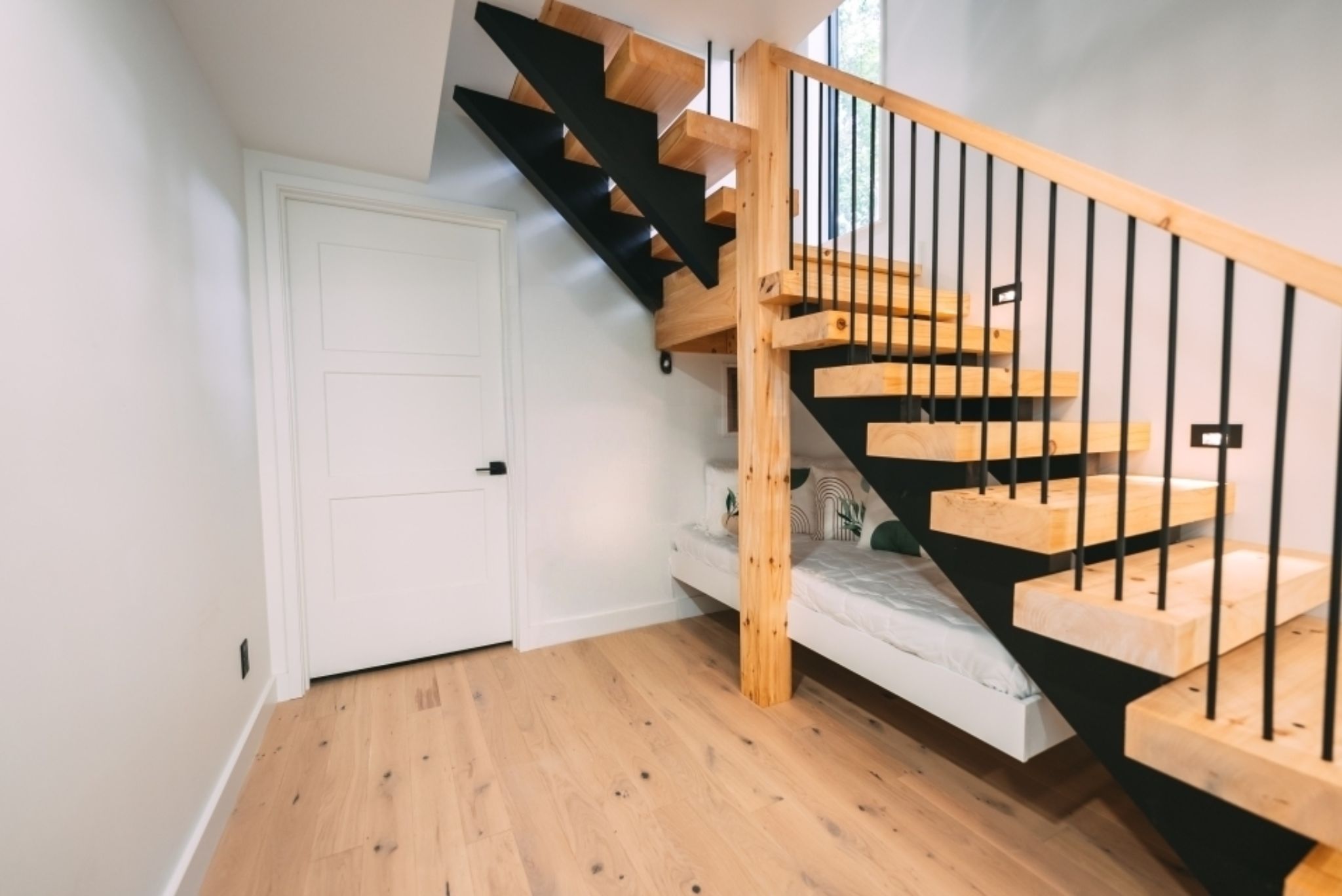 Una escalera de madera con barandillas negras que conduce a un rellano con una puerta blanca.