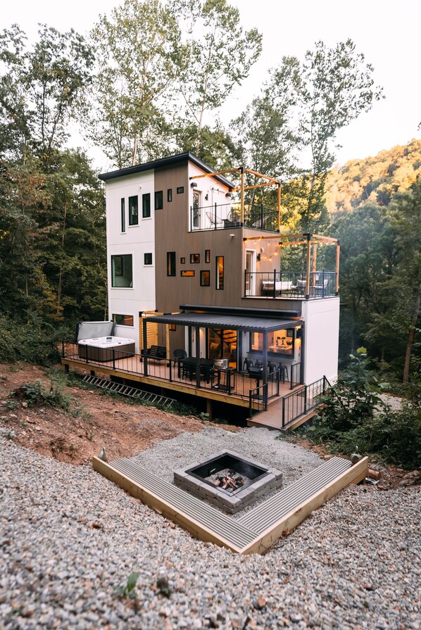 Una casa moderna de varios niveles con terraza, mobiliario exterior y una chimenea.