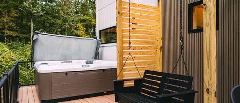 Una terraza de madera con un jacuzzi y una silla colgante.