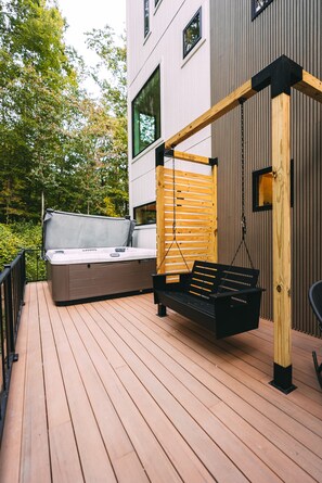 Una terraza de madera con un jacuzzi y una silla colgante.