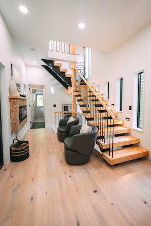 A modern interior with a wooden staircase, a fireplace, and a seating area with chairs.