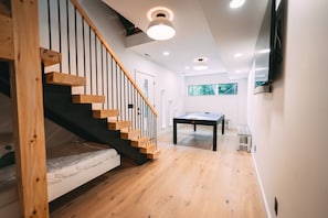 Un intérieur moderne avec un escalier en bois, un lit, une table et un téléviseur fixé au mur.