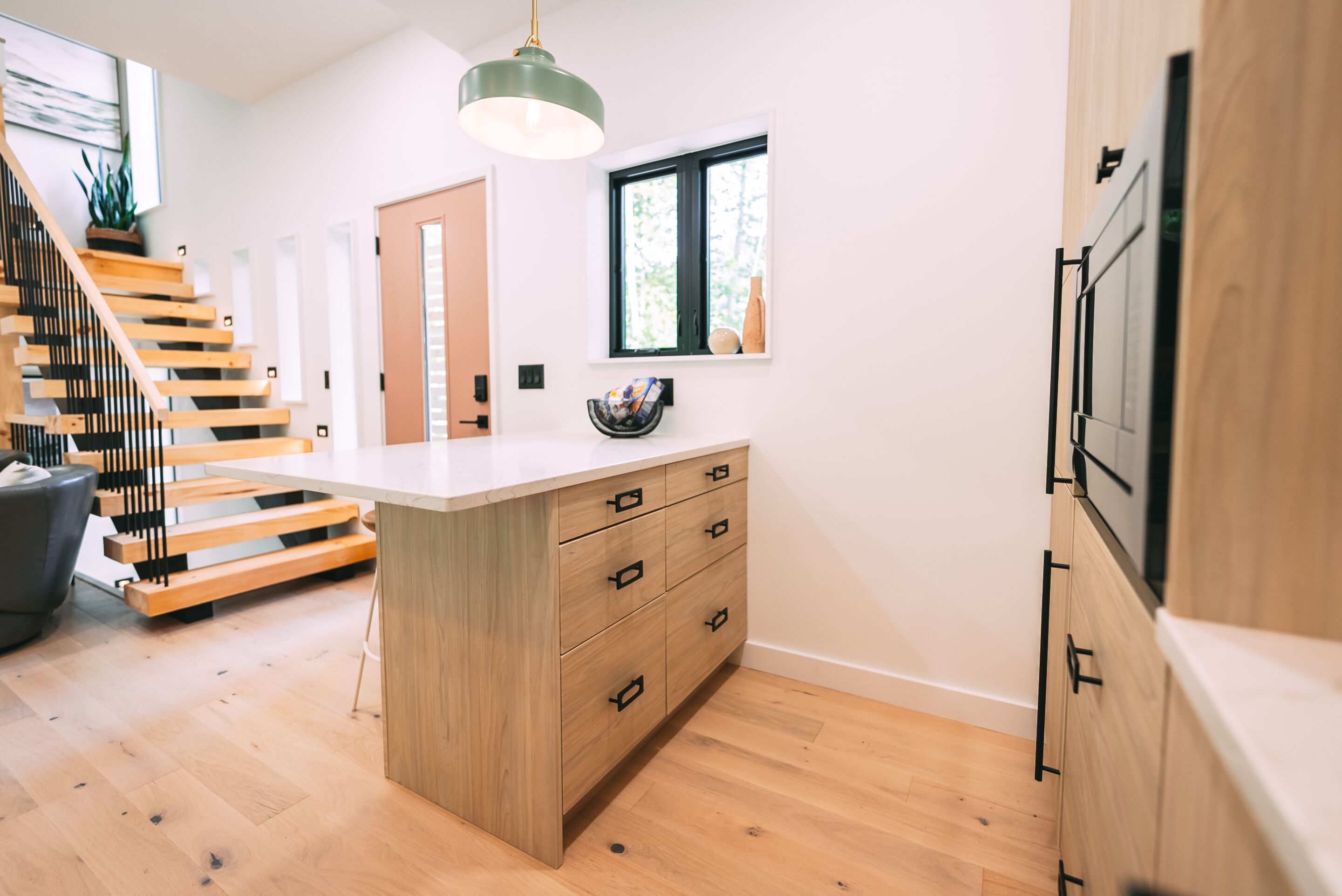 A modern kitchen with a central island, wooden flooring, and a staircase leading to another level.