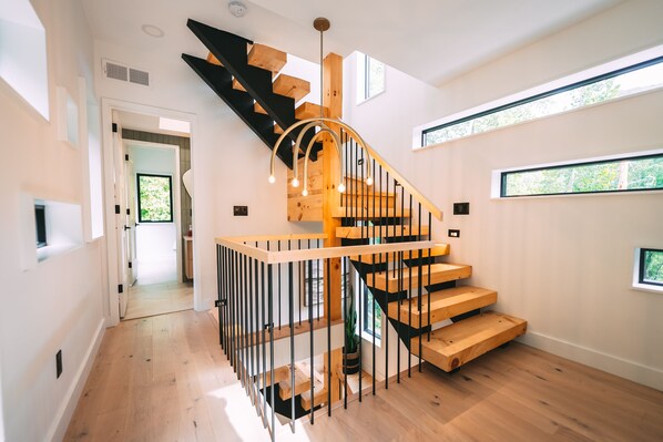 A modern staircase with wooden steps and black railings, leading to a landing with a pendant light fixture.