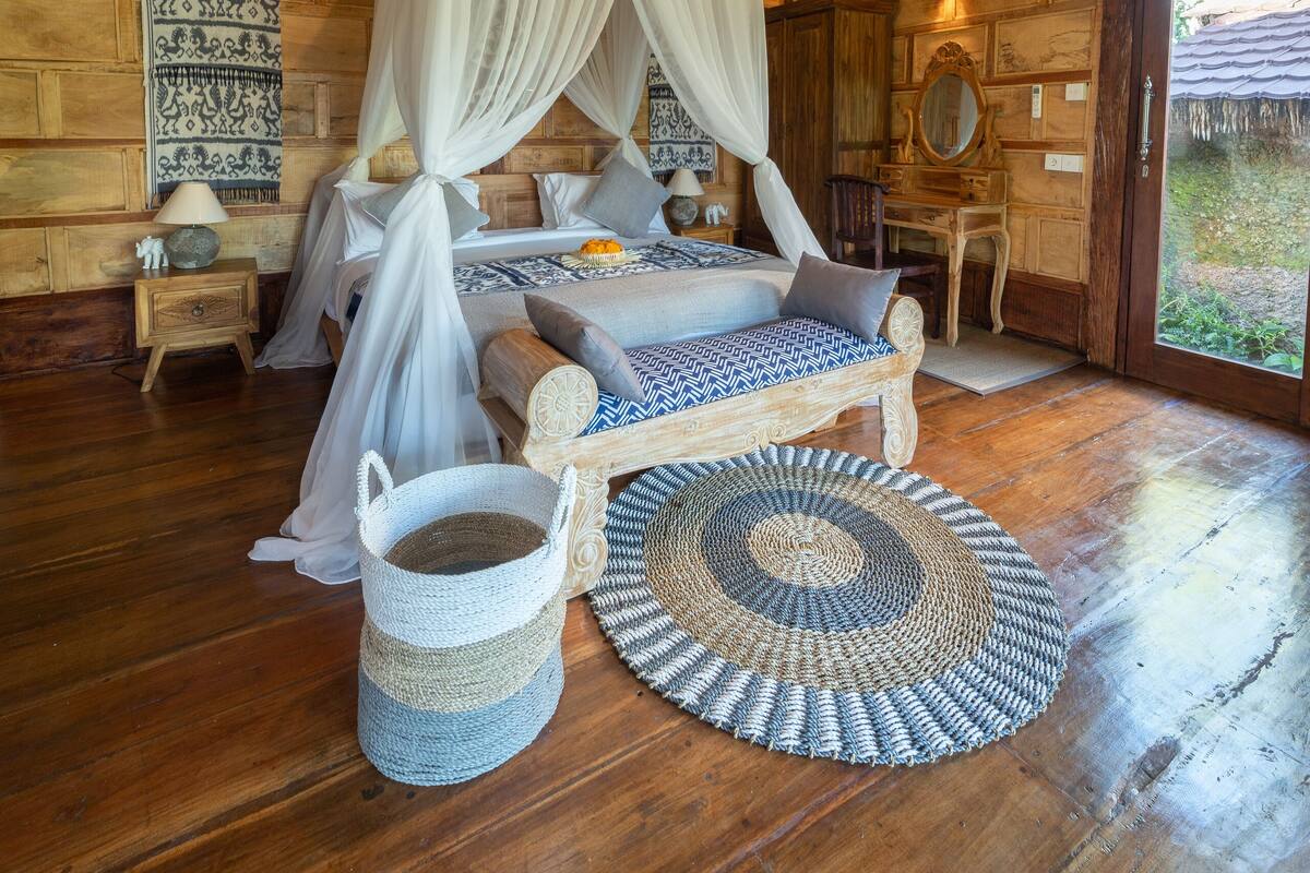 A room with a wooden ceiling, a bed with a canopy, a woven rug, and a wooden dresser.