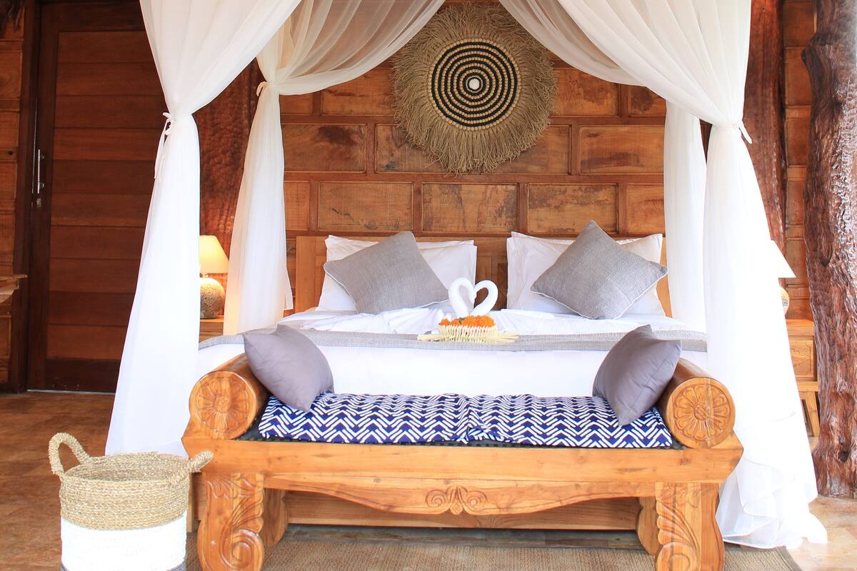 A wooden bed with a canopy, a woven basket, and a patterned rug.