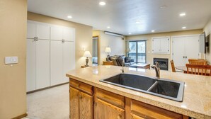 A kitchen with a granite countertop, double sink, wooden cabinets, and a dining area with a table and chairs.