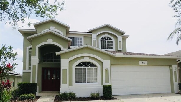 A two-story house with a garage, a front entrance, and a well-maintained lawn. - 5-Bedroom Oasis Near Disney, Golf Paradise and Beach (Davenport)