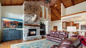 A spacious living room with a stone fireplace, leather sofa, and a large flat-screen TV. - Spacious Home on Beech Mountain w/ Views (Beech Mountain)