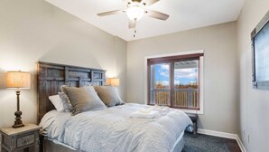 A bedroom with a bed, a ceiling fan, a window with a view, and a nightstand with a lamp. - Spacious Home on Beech Mountain w/ Views (Beech Mountain)