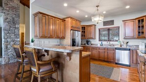 A kitchen with wooden cabinets, a granite countertop, and a built-in island with bar stools. - Spacious Home on Beech Mountain w/ Views (Beech Mountain)