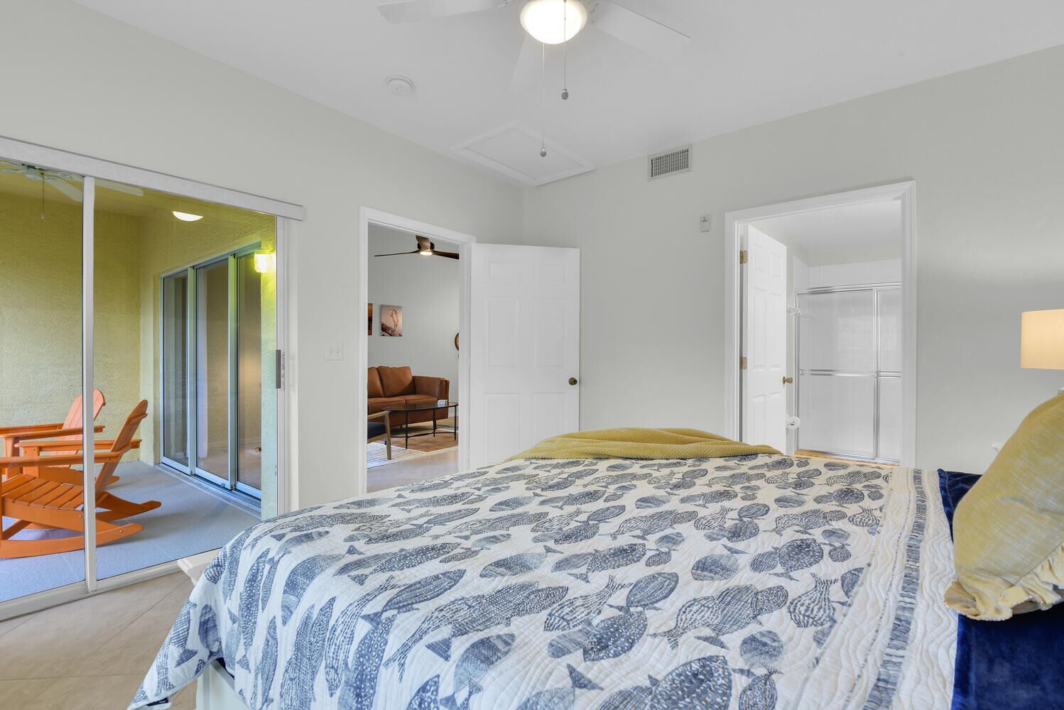 A bedroom with a bed, a sliding glass door leading to a balcony, and a separate living area with a sofa and a coffee table.