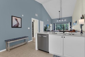 A modern kitchen with a built-in dishwasher, a bench, and a large window overlooking a garden.