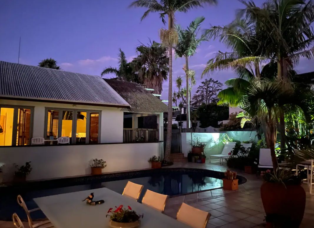 A pool area with lounge chairs, a dining table, and potted plants.