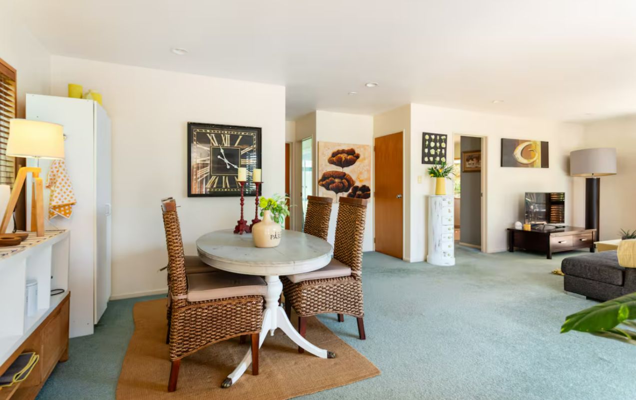 Uma sala de estar moderna com uma mesa de jantar redonda, cadeiras de vime, um relógio na parede e um sofá.
