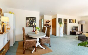 A modern living room with a round dining table, wicker chairs, a clock on the wall, and a sofa.