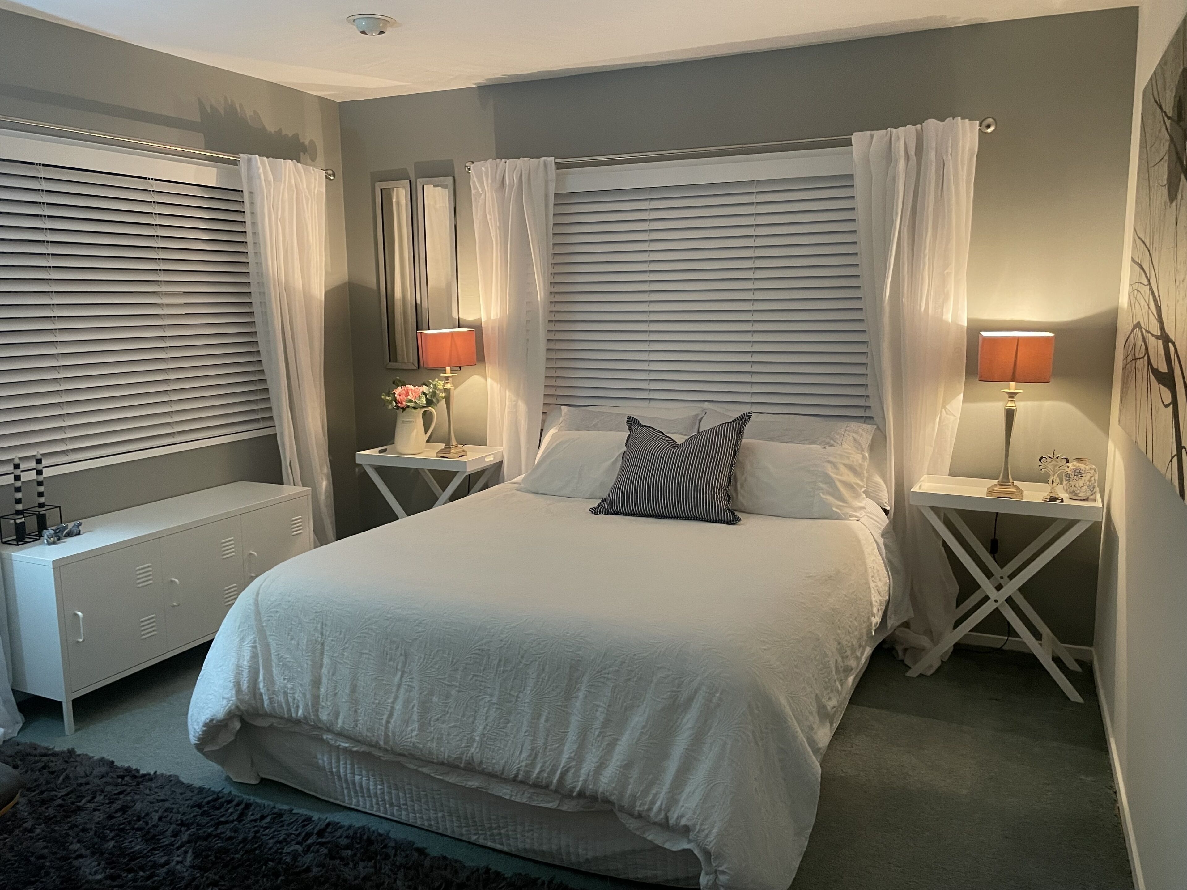 A bedroom with a large bed, two bedside tables with lamps, a dresser, and a radiator.