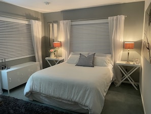 A bedroom with a large bed, two bedside tables with lamps, a dresser, and a radiator.