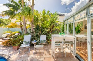An outdoor patio with chairs, a table, and a glass enclosure with a view. - Great-Located North Shore Room in Tropical Garden – Close to the Beach 🌴🌊 (Auckland)