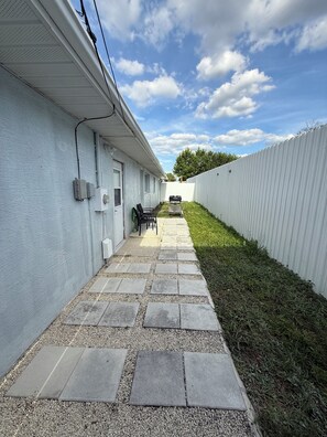 A narrow paved pathway leading to a building with a white exterior, a white fence on one side, and a clear sky with clouds. - Cozy little apartment in Sprin Hill! (Spring Hill)