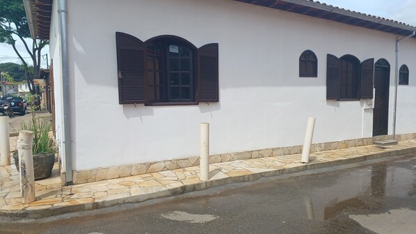 A building with a white exterior, multiple windows with dark shutters, and a stone-paved entrance area.