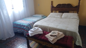 Une chambre avec deux lits, une tête de lit en bois, un banc avec des serviettes et des rideaux à motifs.