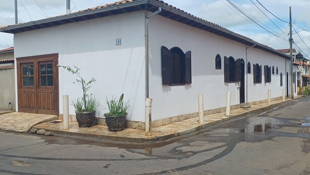 Un bâtiment blanc avec une porte marron, des volets noirs et des plantes en pot.