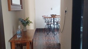 Un couloir avec une table en bois et une chaise, un petit vase avec des fleurs et un miroir au mur.
