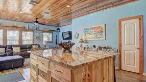 A spacious living area with a wooden ceiling, a large wooden island with drawers, a leather sofa, and a television on the wall. - Private Heated Pool and 2 Golf Carts Included, Pet Friendly (Port Aransas)