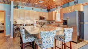 A kitchen with wooden cabinets, a central island, bar stools, a refrigerator, and a washing machine. - Private Heated Pool and 2 Golf Carts Included, Pet Friendly (Port Aransas)