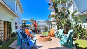 A patio area with outdoor seating, a fire pit, and lush tropical plants. - Private Heated Pool and 2 Golf Carts Included, Pet Friendly (Port Aransas)
