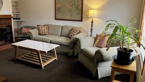 A cozy living room with a sofa set, a coffee table, a map on the wall, a lamp, and a potted plant.