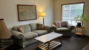 A living room with a sofa, armchair, coffee table, lamp, and a map on the wall.