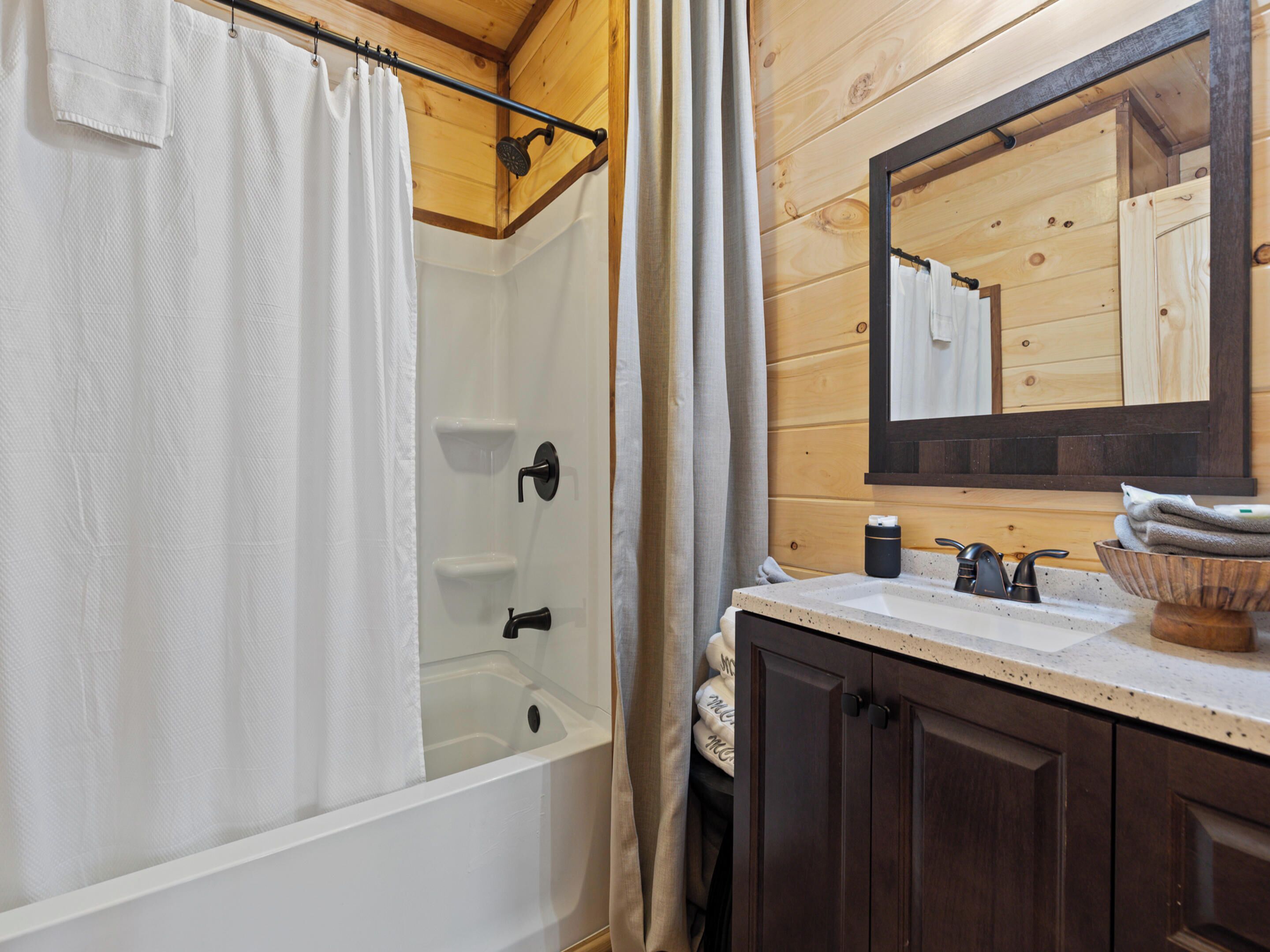 A bathroom with a bathtub, a shower, a sink, a mirror, and wooden paneling.