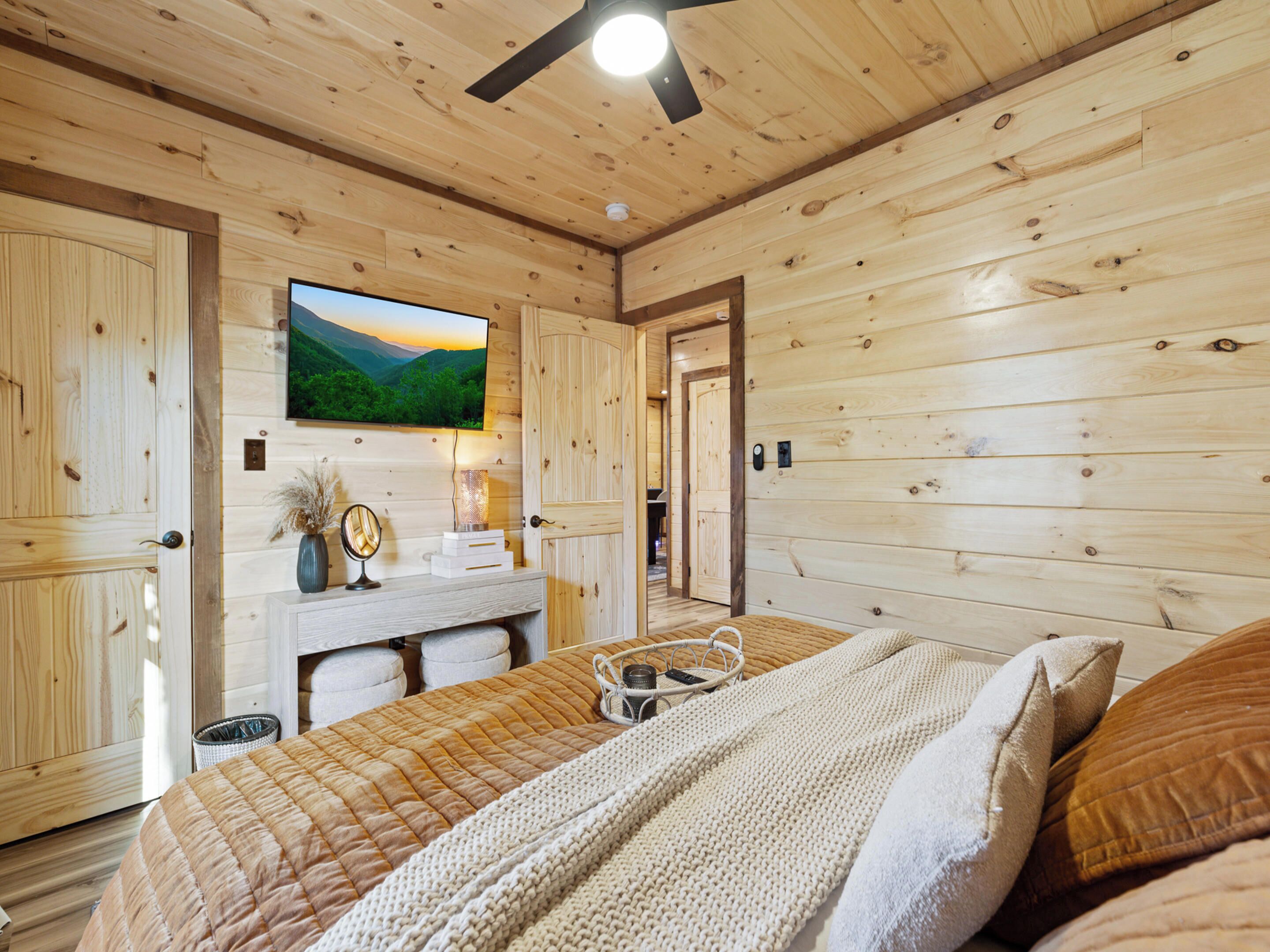 A wooden cabin bedroom with a bed, bedside table, and a television mounted on the wall.