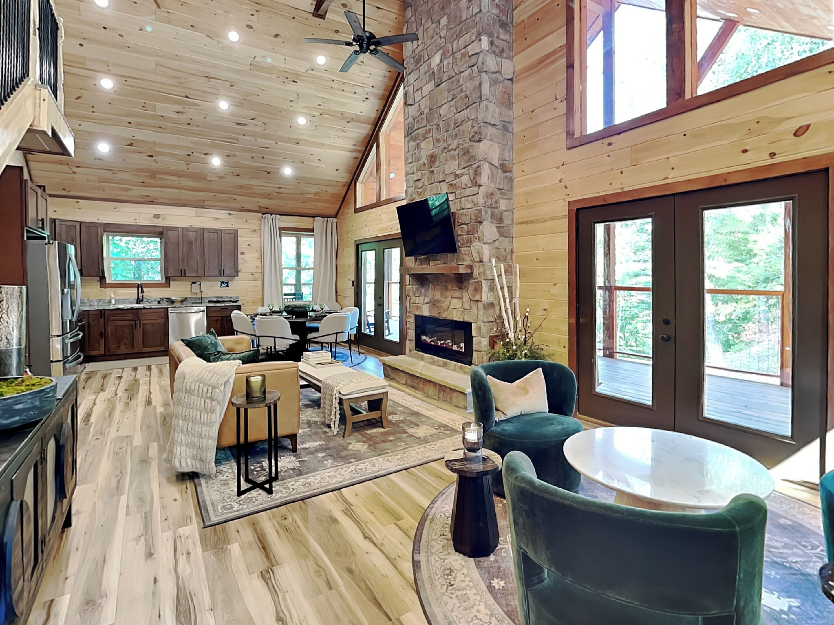 A spacious living area with a stone fireplace, wooden ceiling, and large windows.