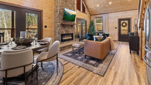A spacious living area with a fireplace, comfortable seating, and large windows offering views of the outdoors. - Mountain Ventures by Jackson Mountain Rentals (Pigeon Forge)