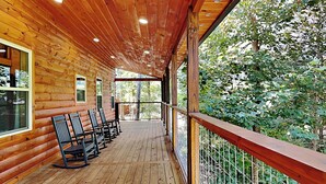 A wooden cabin with a covered porch, wooden flooring, and a view of the surrounding forest. - Mountain Ventures by Jackson Mountain Rentals (Pigeon Forge)