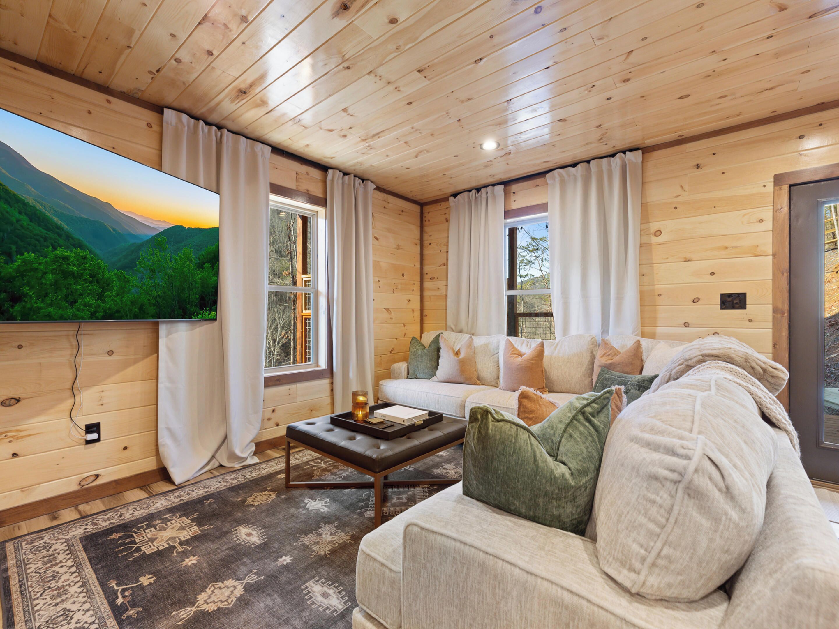 Un acogedor interior de cabaña con una televisión grande, paredes de madera, un sofá y una alfombra.