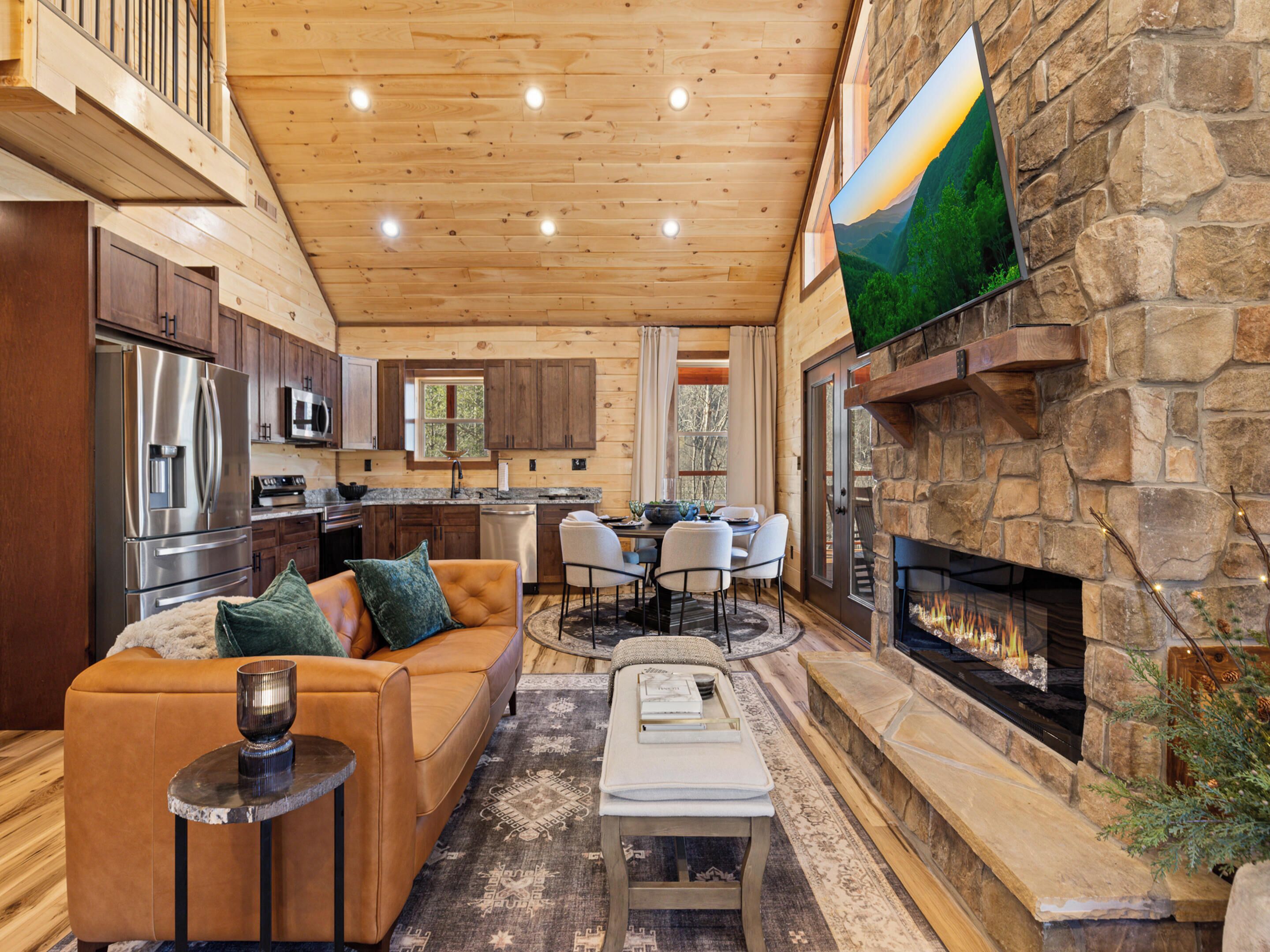 A spacious living area with a stone fireplace, wooden ceiling, and a large TV mounted on the wall.
